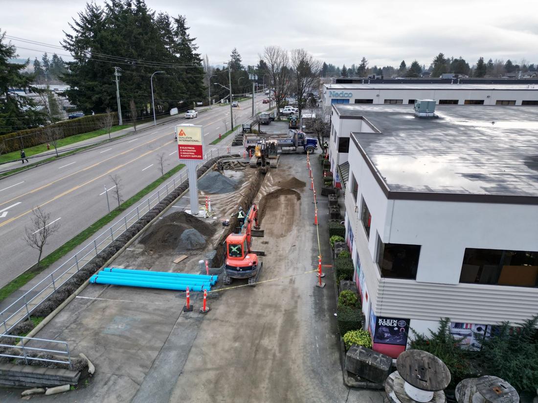 Drone view of water main work along a commercial roadway, with blue pipe staged